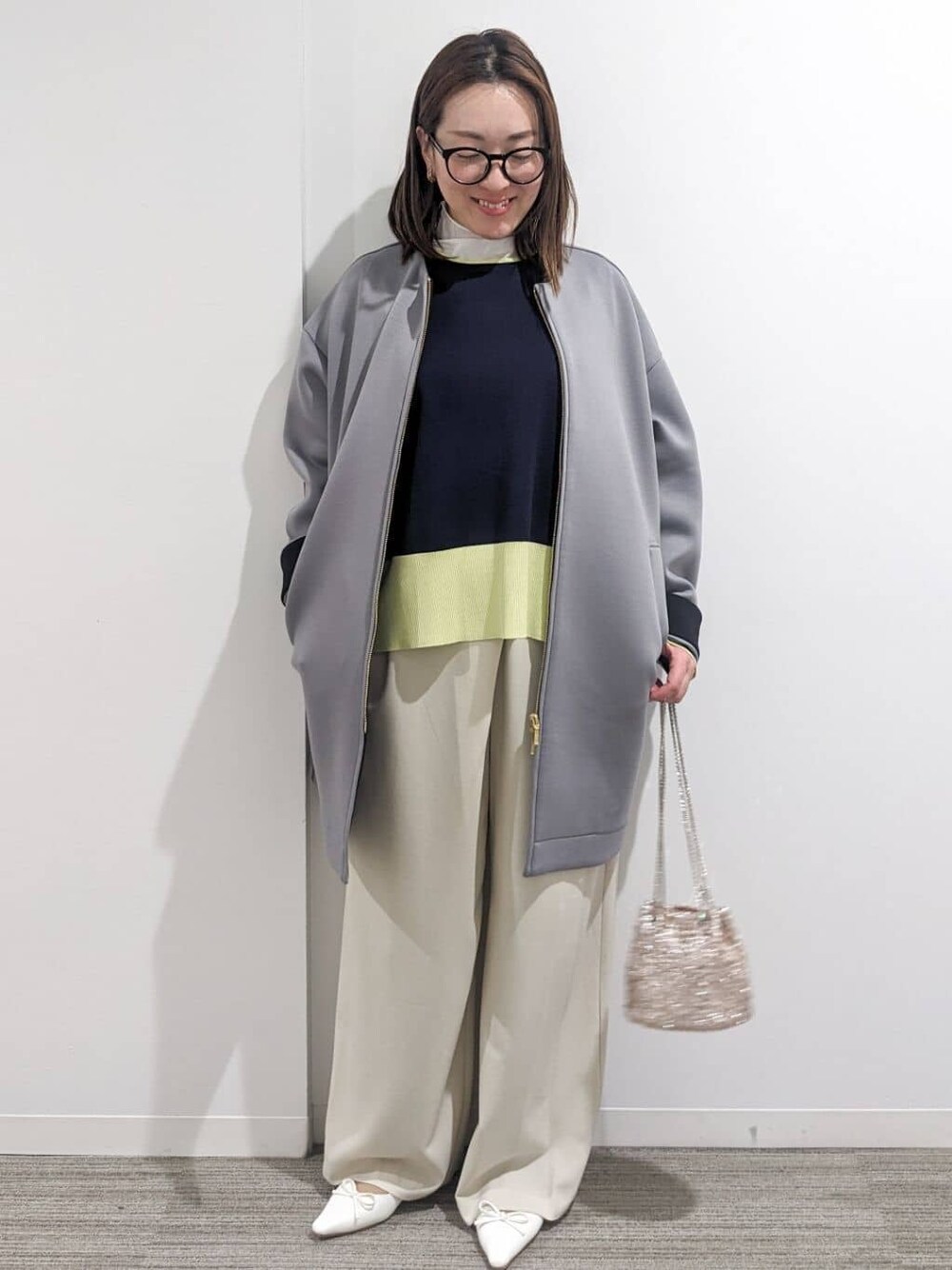 グレー系のノーカラーコート、ブルー系のニット/セーター、ホワイト系のTシャツ/カットソーを着用したレディースの春コーディネートの1枚目の写真
