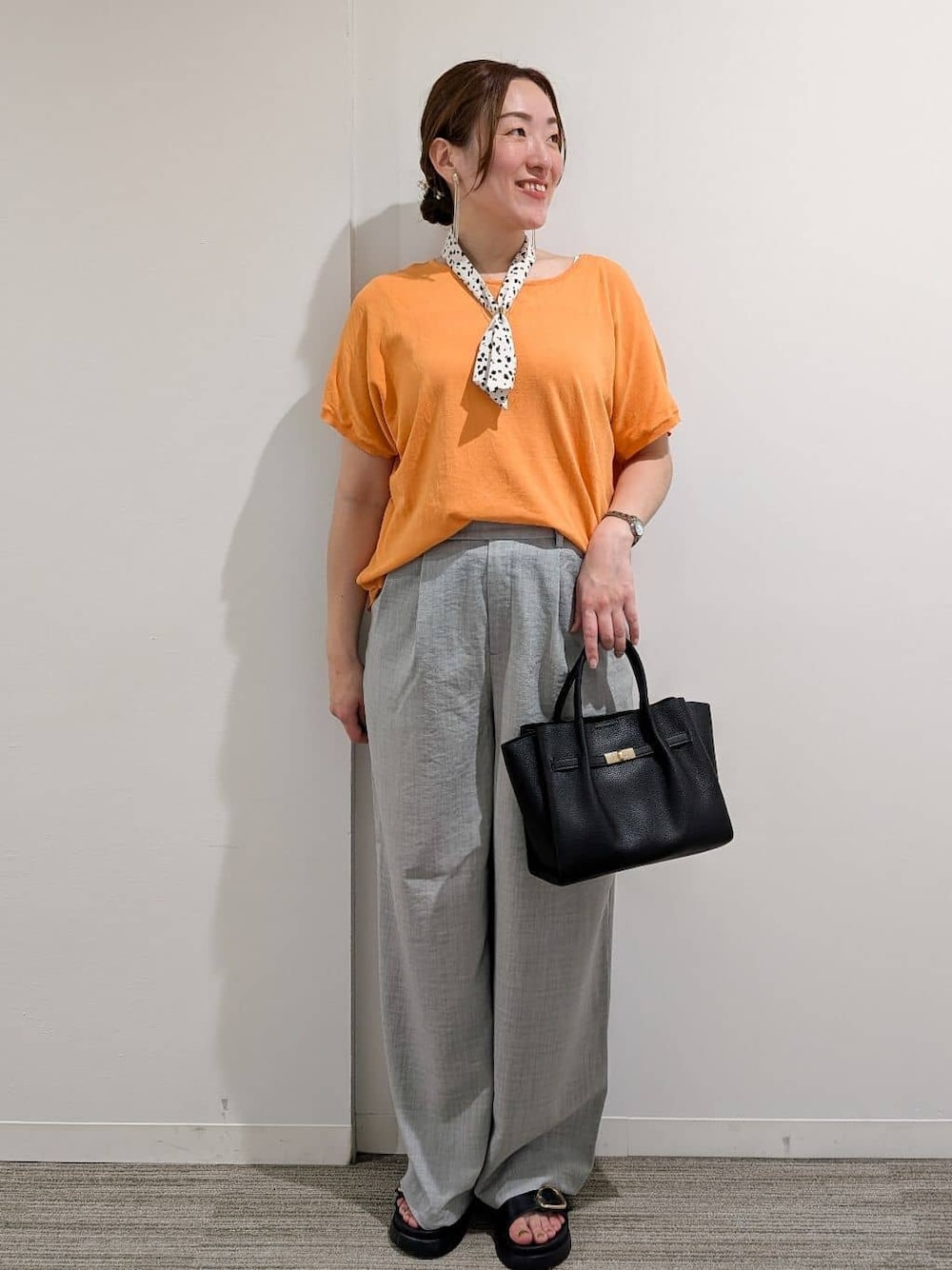 オレンジ系のニット/セーター、グレー系のその他パンツ、ブラック系のサンダルを着用したレディースの夏コーディネートの1枚目の写真