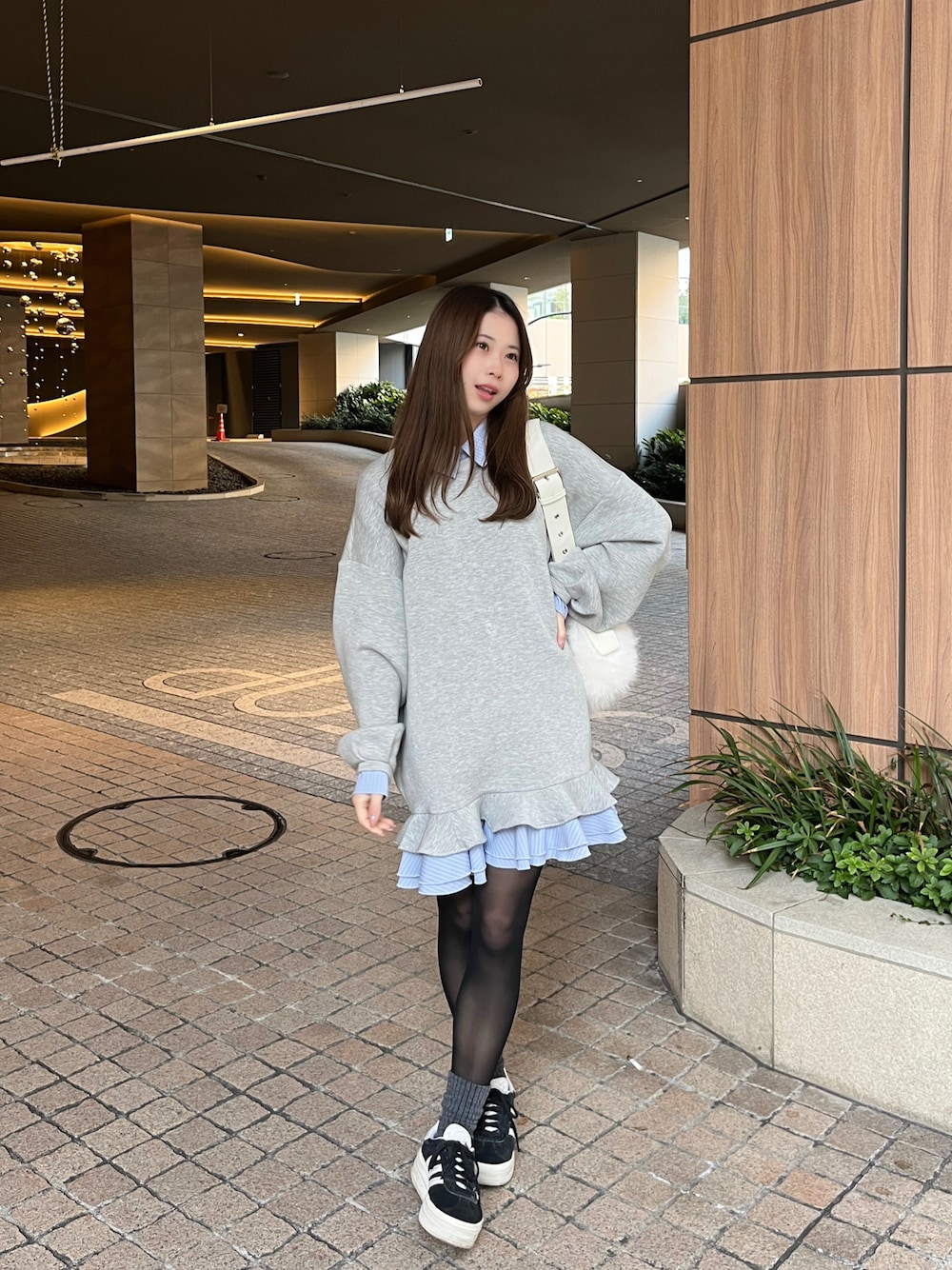 ブラック系のスニーカー、グレー系のスウェット、ホワイト系のショルダーバッグを着用したレディースの冬コーディネートの1枚目の写真