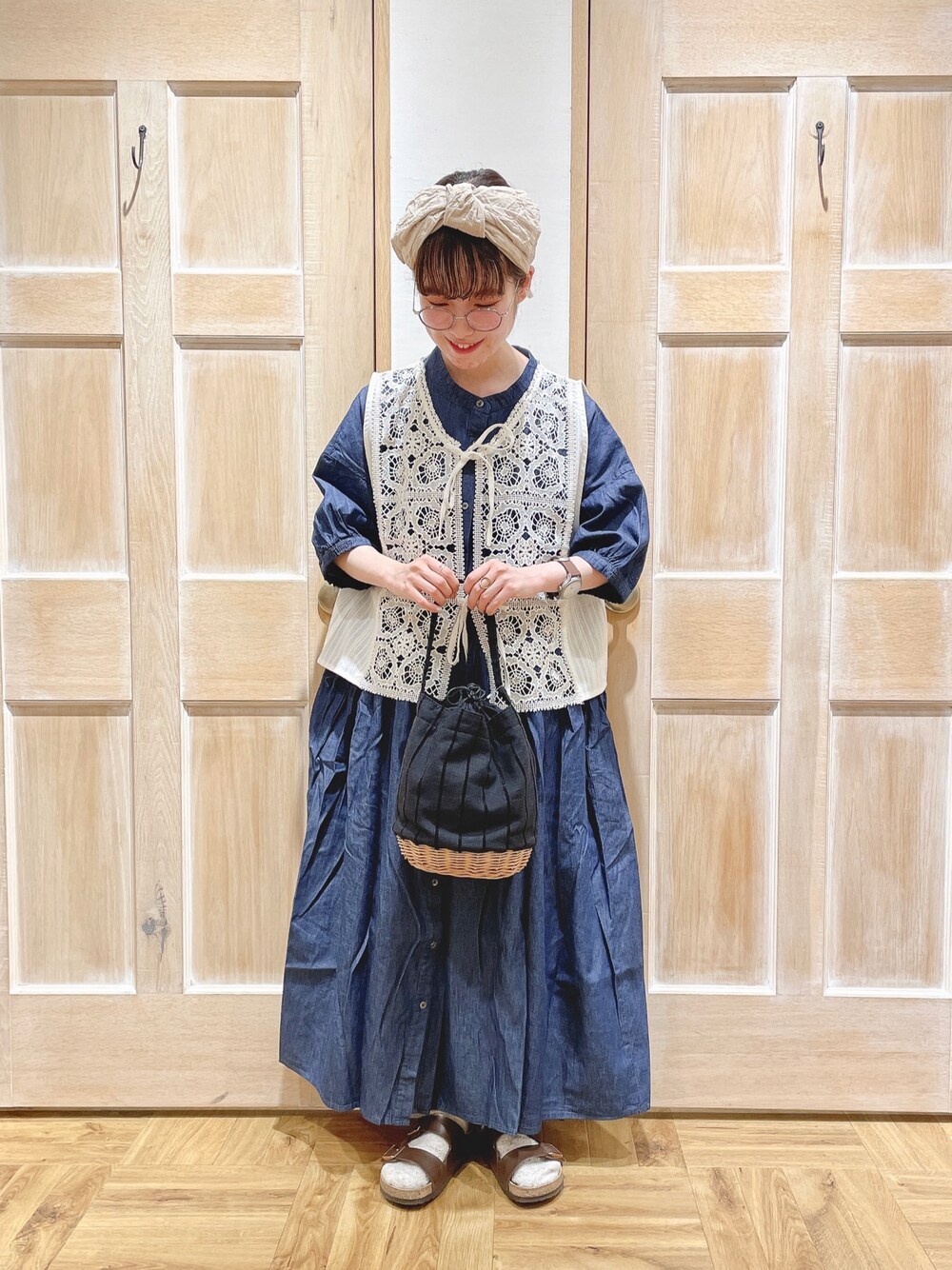 ホワイト系のベスト、ブラック系のかごバッグ、ブラウン系のサンダルを着用したレディースの夏コーディネートの1枚目の写真