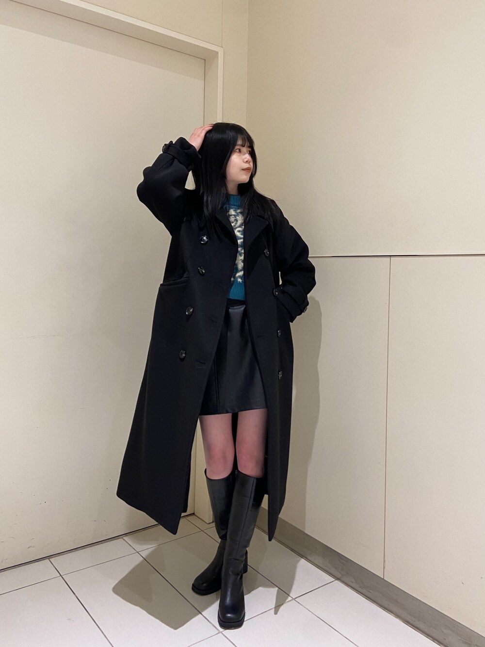 グリーン系のニット/セーター、ブラック系のチェスターコート、ブラック系のスカートを着用したレディースの冬コーディネートの1枚目の写真