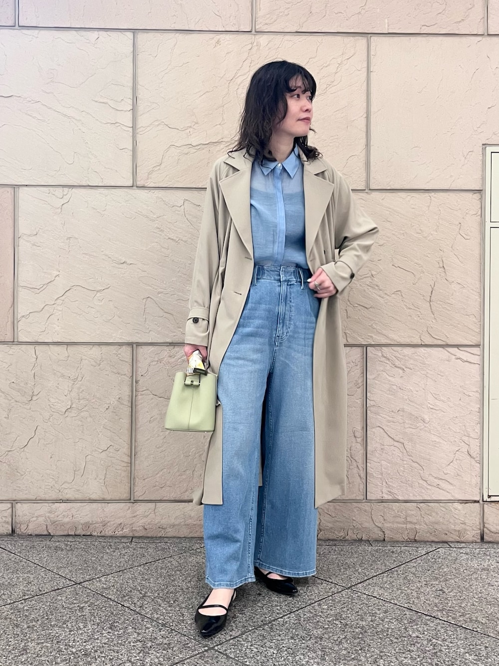 ブルー系のデニムパンツ、ベージュ系のトレンチコート、グリーン系のショルダーバッグを着用したレディースの春コーディネートの1枚目の写真