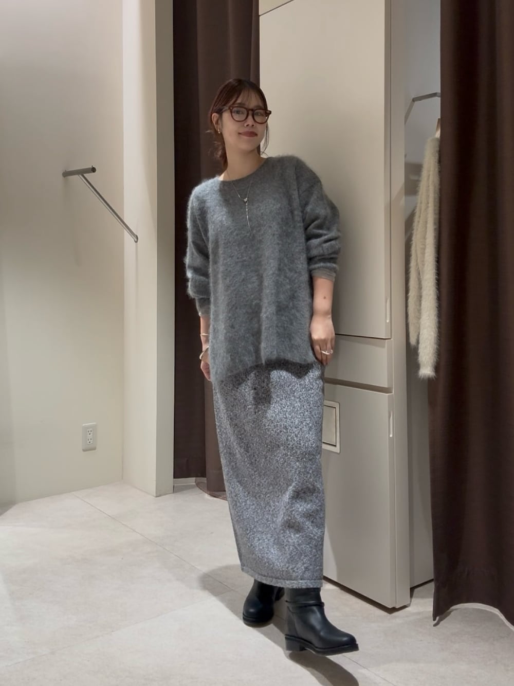 グレー系のニット/セーター、グレー系のスカート、ブラック系のブーツを着用したレディースの秋コーディネートの1枚目の写真