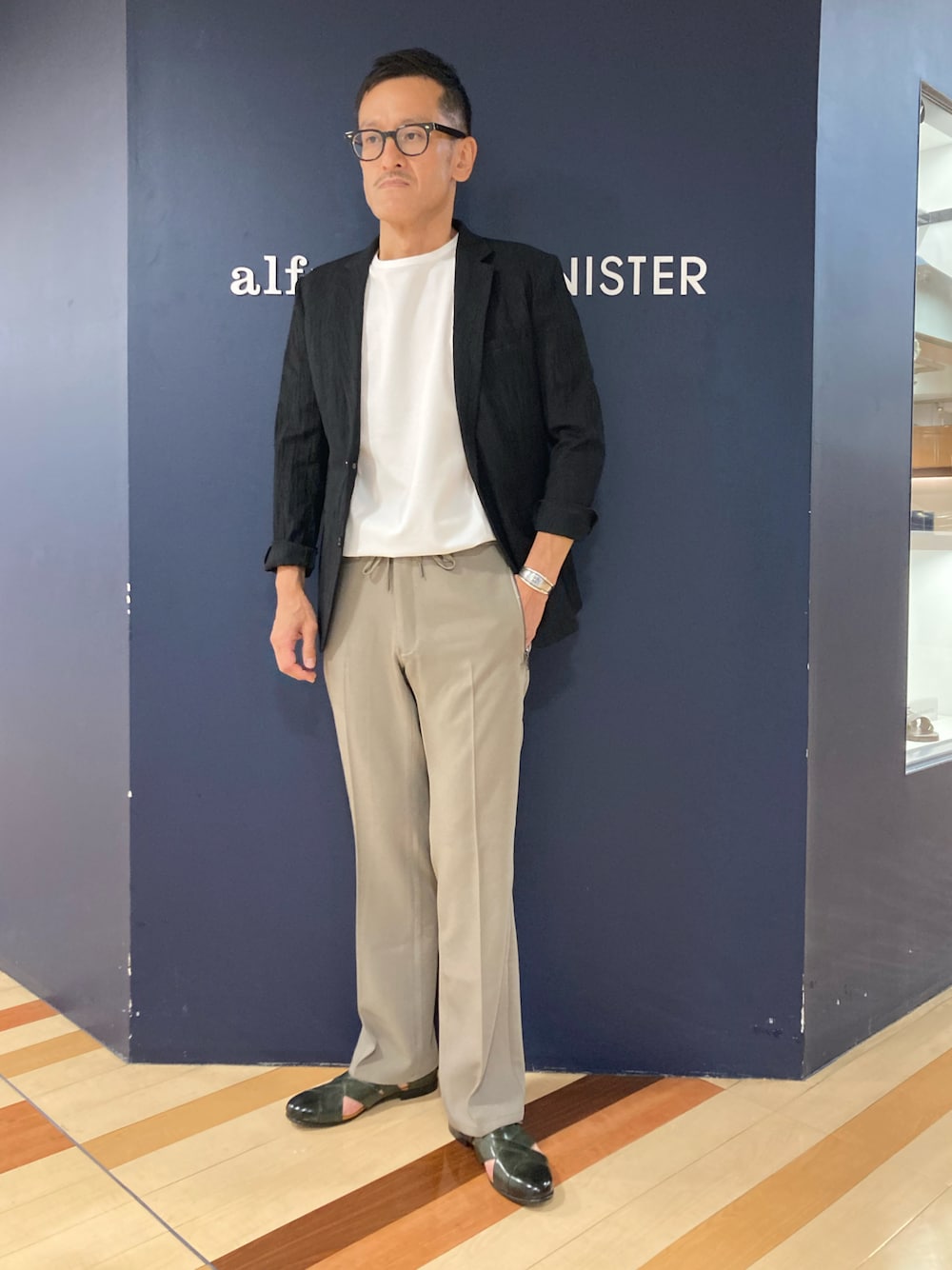 ブラック系のテーラードジャケット、ホワイト系のTシャツ/カットソー、グリーン系のスラックスを着用したメンズの春コーディネートの1枚目の写真