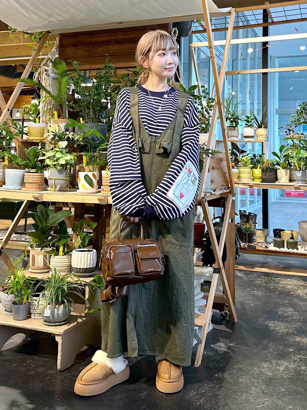 グリーン系のジャンパースカート、その他のTシャツ/カットソー、ブラウン系のショルダーバッグを着用したレディースの秋コーディネートの1枚目の写真