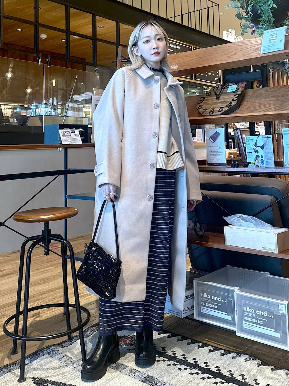 ベージュ系のステンカラーコート、ブラック系のブーツ、ブルー系のスカートを着用したレディースの冬コーディネートの1枚目の写真