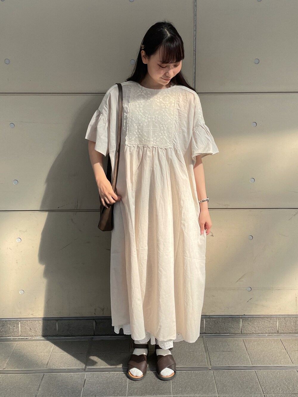 ホワイト系のワンピース、ブラウン系のハンドバッグ、ブラウン系のサンダルを着用したレディースの春コーディネートの1枚目の写真