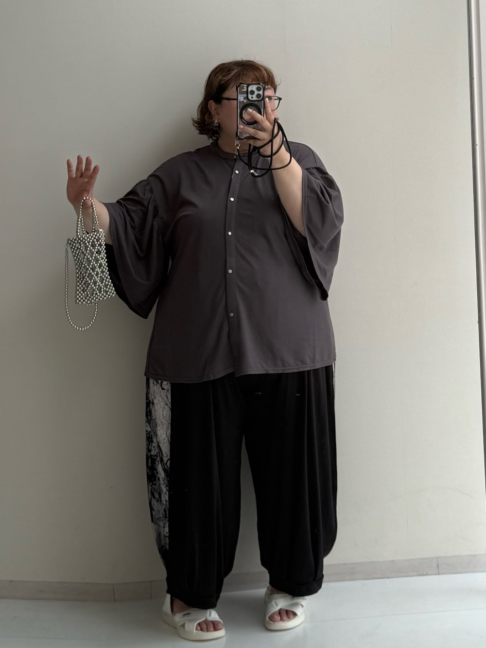シルバー系のショルダーバッグ、ブラック系のパンツ、ホワイト系のサンダルを着用したレディースの夏コーディネートの1枚目の写真