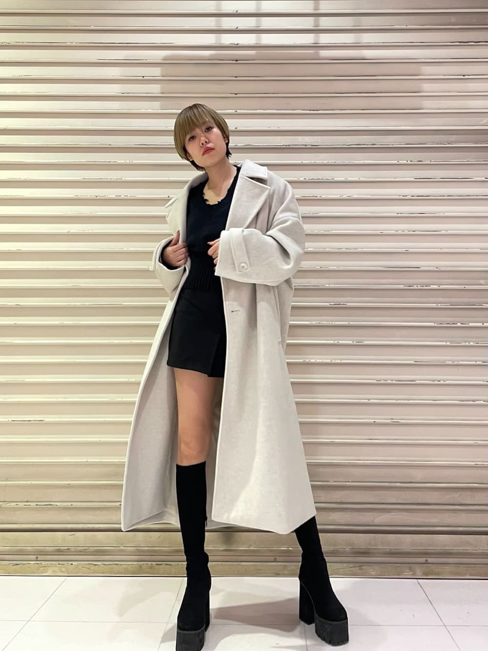 ホワイト系のチェスターコート、ブラック系のスカート、ブラック系のブーツを着用したレディースの冬コーディネートの1枚目の写真