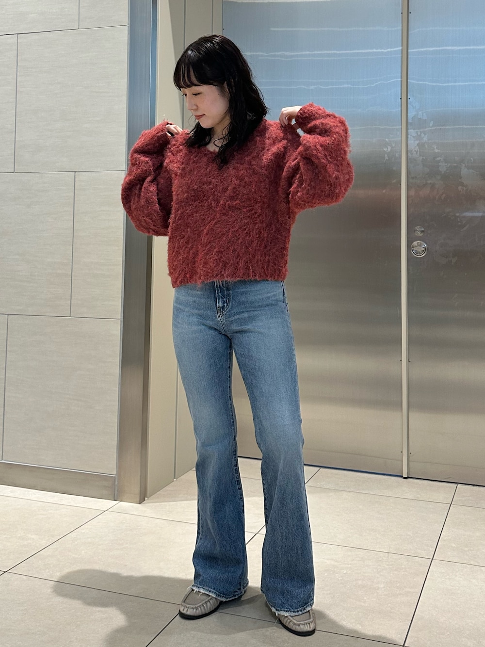 レッド系のニット/セーター、ブルー系のデニムパンツを着用したレディースの秋コーディネートの1枚目の写真