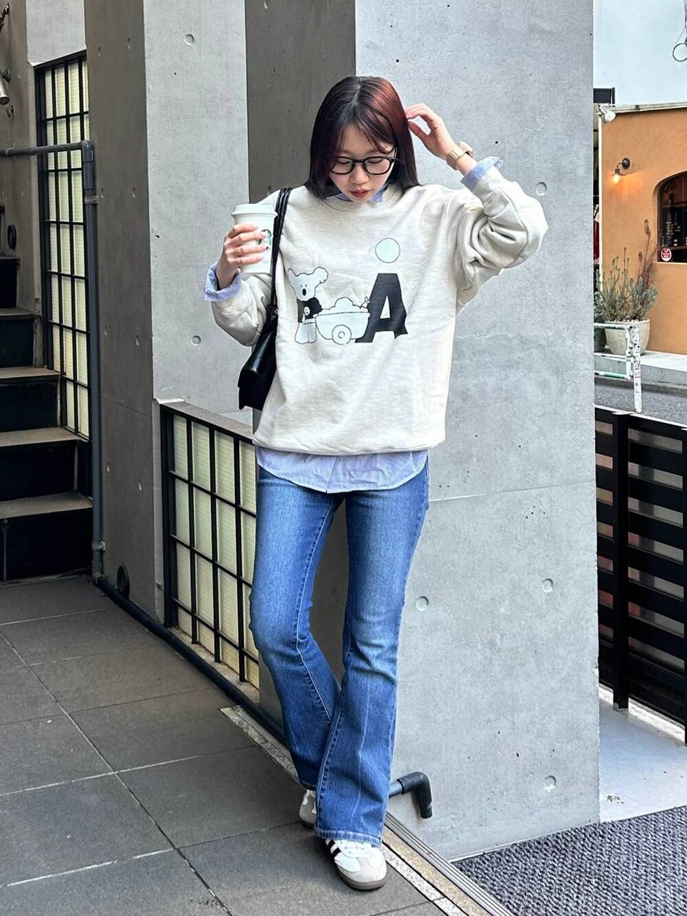 ブルー系のデニムパンツ、ブラック系のショルダーバッグ、ベージュ系のスウェットを着用したレディースの冬コーディネートの1枚目の写真