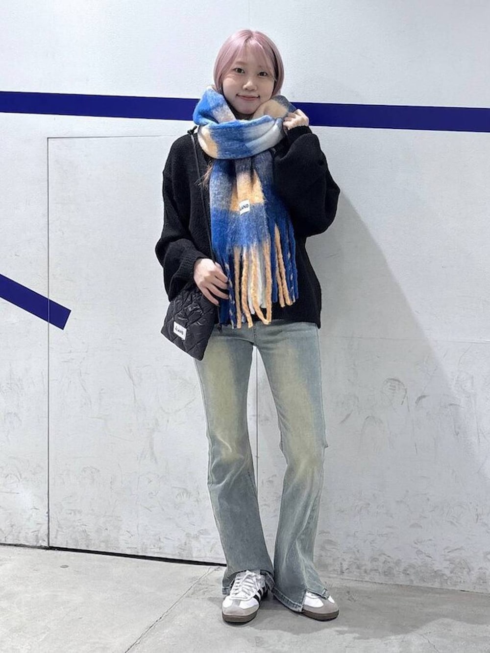 ブルー系のデニムパンツ、ブラック系のニット/セーター、ブラック系のショルダーバッグを着用したレディースの秋コーディネートの1枚目の写真