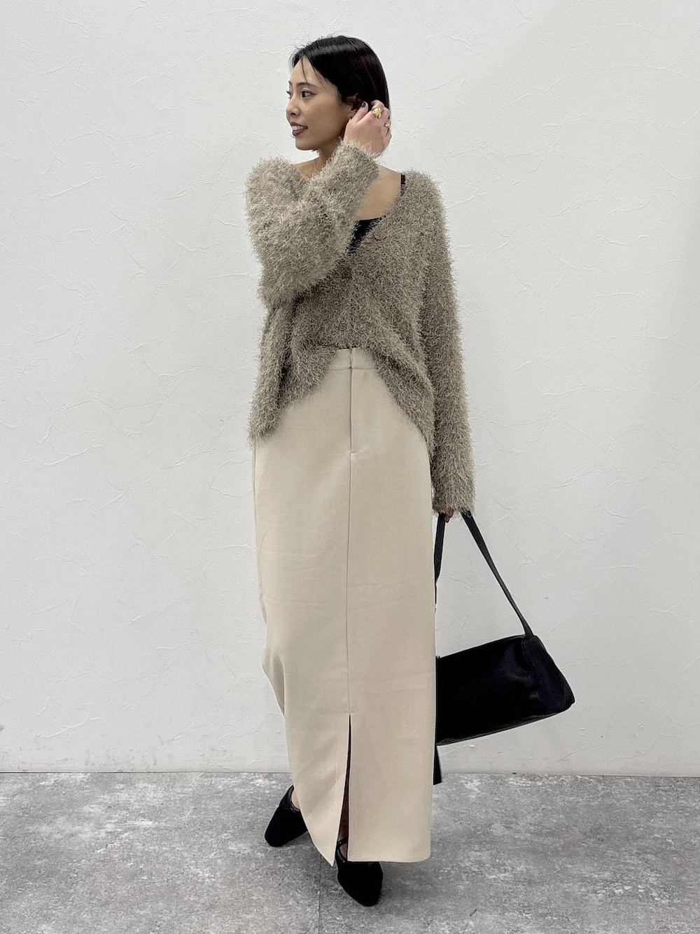 ブラック系のショルダーバッグ、ベージュ系のスカート、ゴールド系のピアス(両耳用)を着用したレディースの冬コーディネートの1枚目の写真