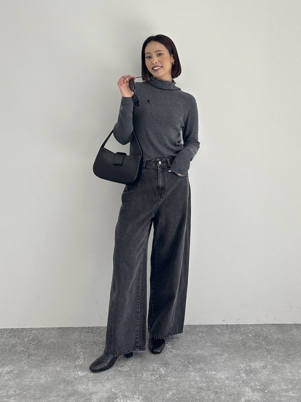 ブラック系のデニムパンツ、ブラック系のブーツ、グレー系のニット/セーターを着用したレディースの秋コーディネートの1枚目の写真