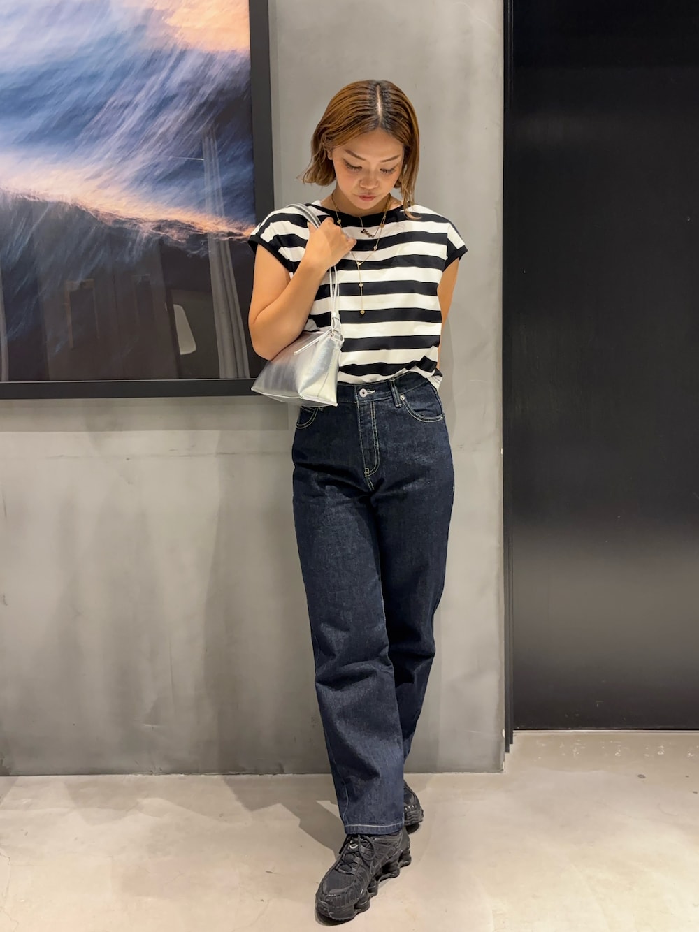 シルバー系のショルダーバッグ、ブラック系のTシャツ/カットソー、ブルー系のデニムパンツを着用したレディースの夏コーディネートの1枚目の写真