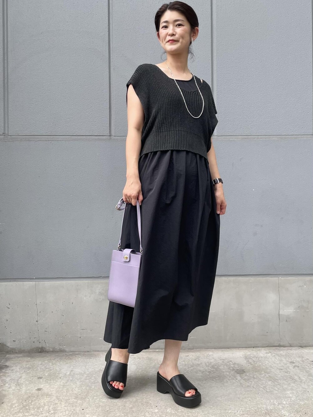 パープル系のショルダーバッグ、ブラック系のサンダル、ブラック系のワンピースを着用したレディースの夏コーディネートの1枚目の写真