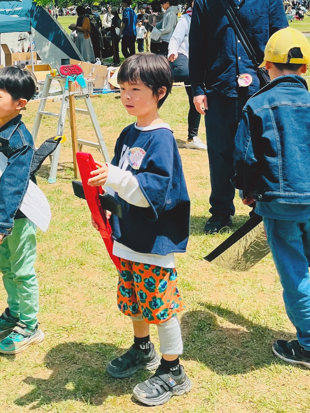 オレンジ系のパンツ、ブラック系のスニーカー、ブルー系のスウェットを着用したキッズの春コーディネートの1枚目の写真