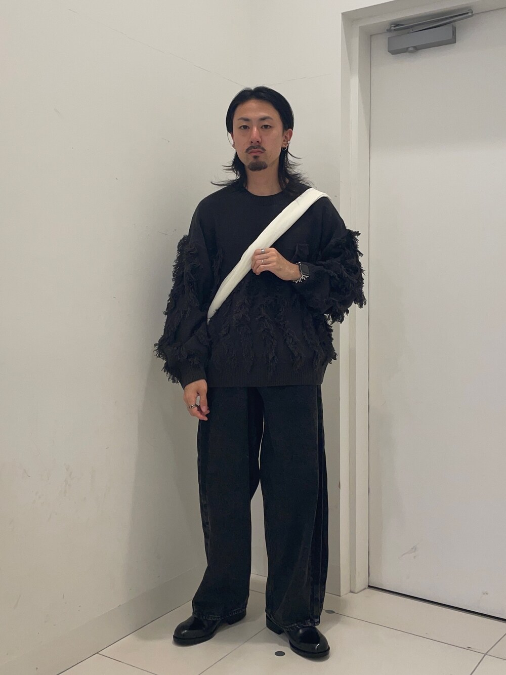 ブラック系のデニムパンツ、グレー系のニット/セーター、ホワイト系のショルダーバッグを着用したメンズの秋コーディネートの1枚目の写真