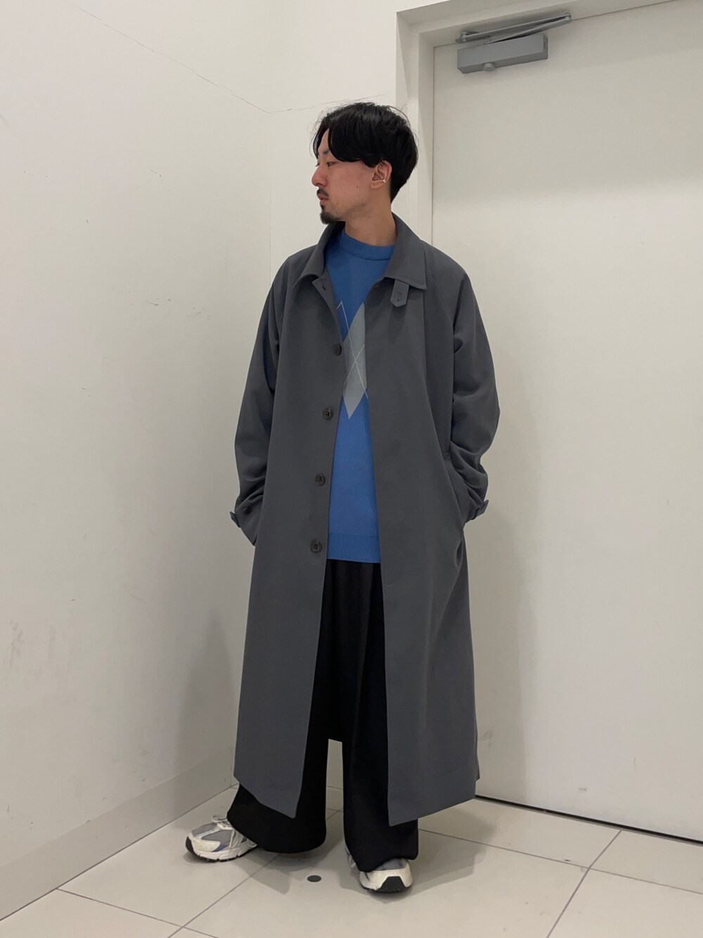 ブラック系のスラックス、ブルー系のニット/セーター、ブルー系のステンカラーコートを着用したメンズの冬コーディネートの1枚目の写真