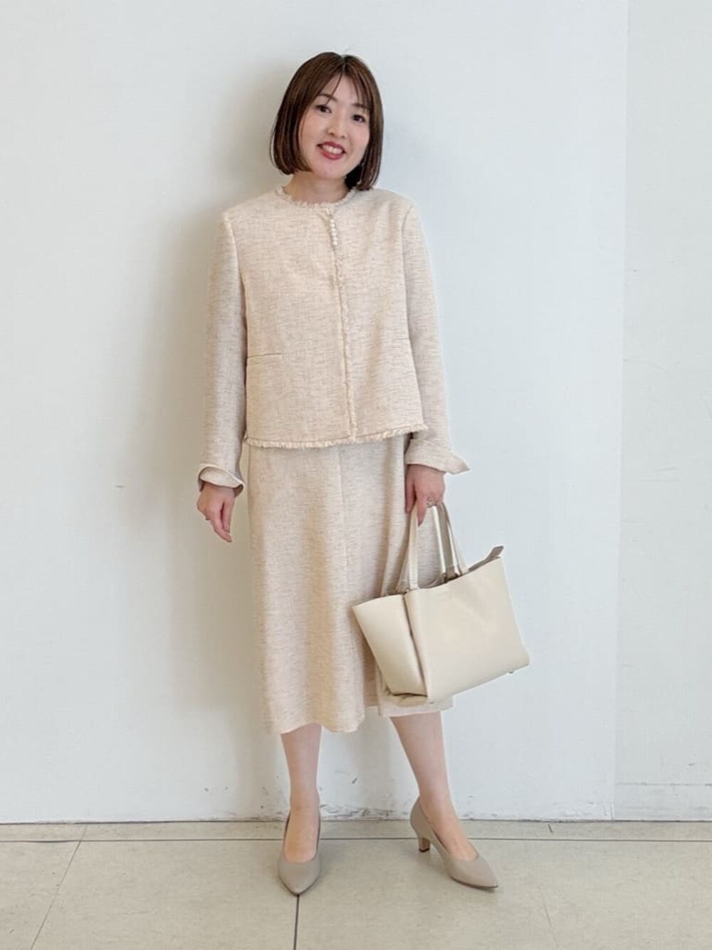 ベージュ系のハンドバッグ、ベージュ系のワンピース、ベージュ系のノーカラージャケットを着用したレディースの春コーディネートの1枚目の写真