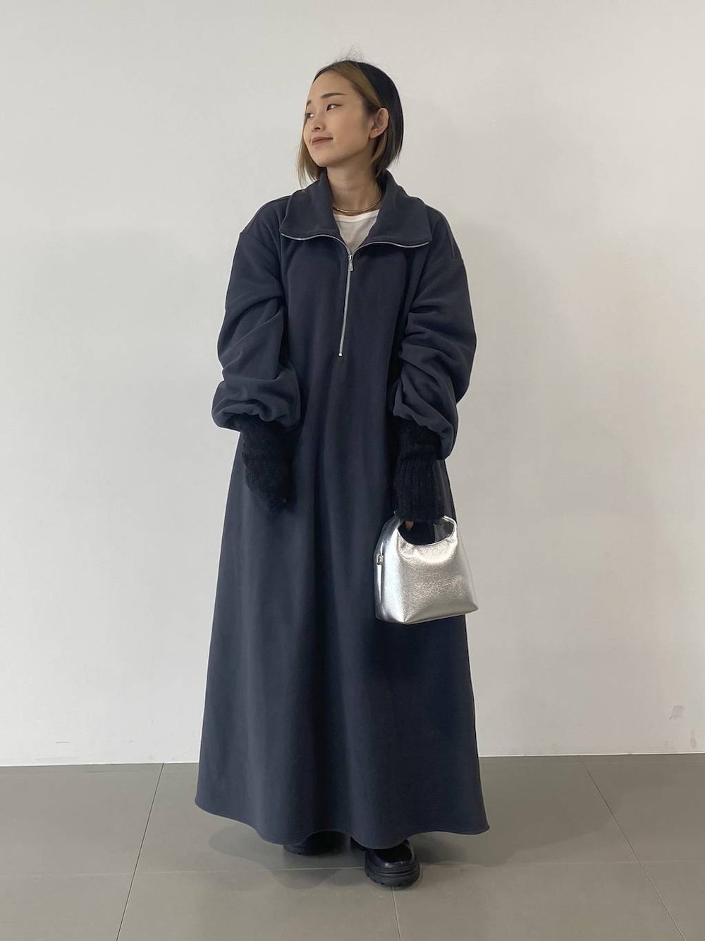 シルバー系のショルダーバッグ、ブラック系のブーツ、グレー系のワンピースを着用したレディースの秋コーディネートの1枚目の写真