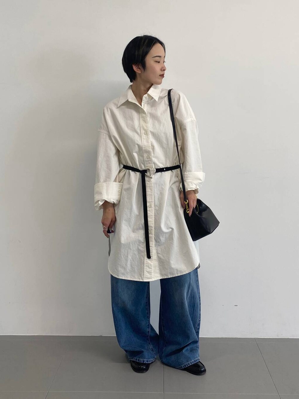 ブルー系のデニムパンツ、ホワイト系のシャツワンピース、ブラック系のベルトを着用したレディースの冬コーディネートの1枚目の写真