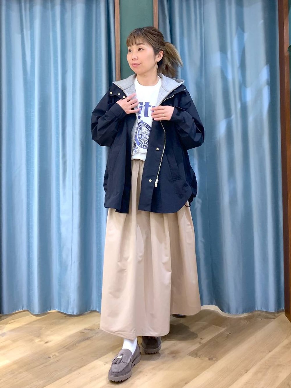 グレー系のローファー、グレー系のパーカー、ベージュ系のスカートを着用したレディースの春コーディネートの1枚目の写真