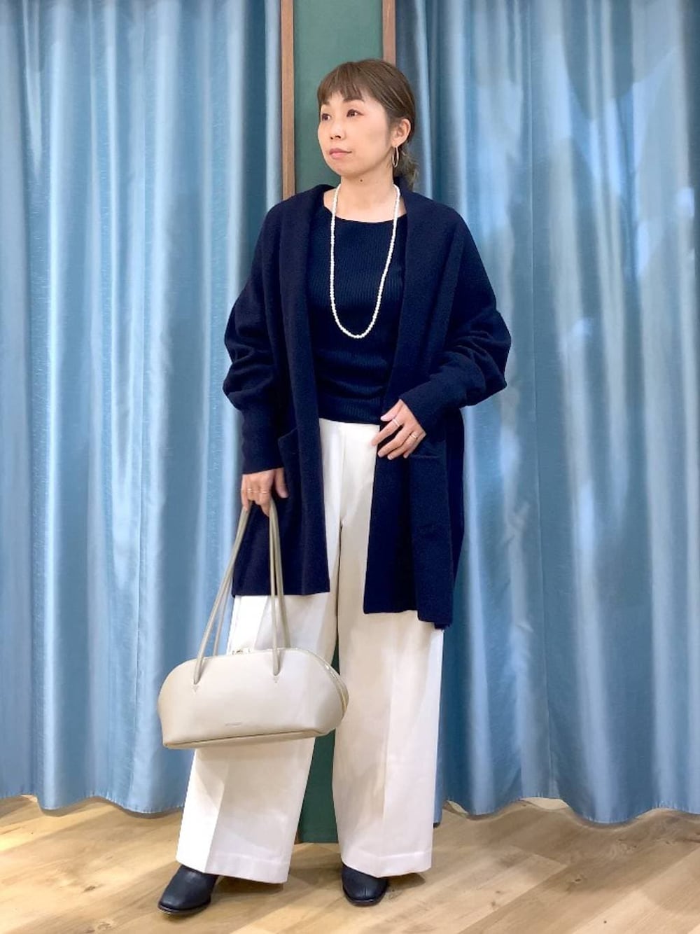 ベージュ系のトートバッグ、ブラック系のブーツ、ブルー系のニット/セーターを着用したレディースの冬コーディネートの1枚目の写真