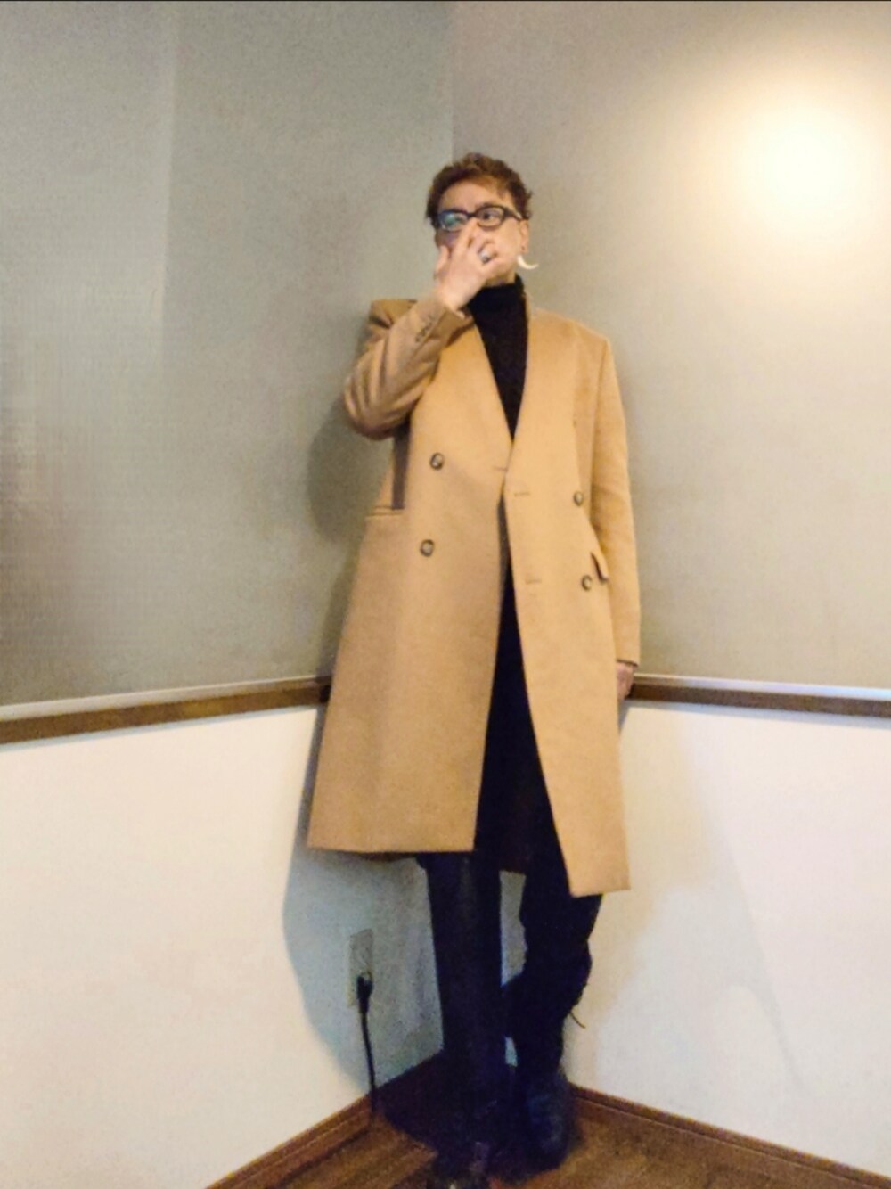 ベージュ系のチェスターコート、ブラック系のデニムパンツ、ブラック系のブーツを着用したメンズの秋コーディネートの1枚目の写真
