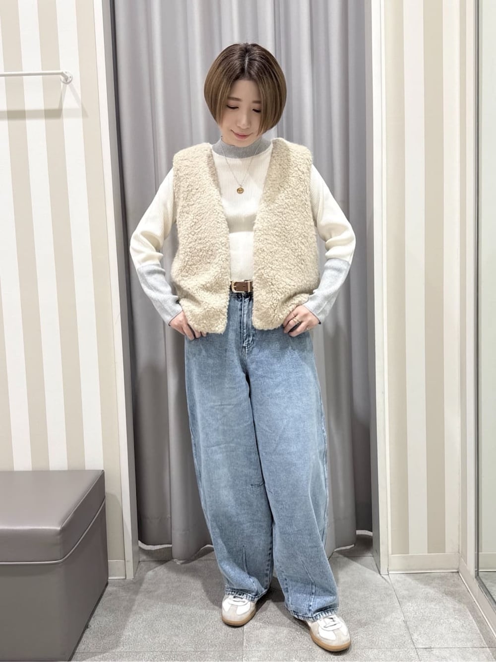 ベージュ系のベスト、グレー系のニット/セーター、ブルー系のデニムパンツを着用したレディースの秋コーディネートの1枚目の写真