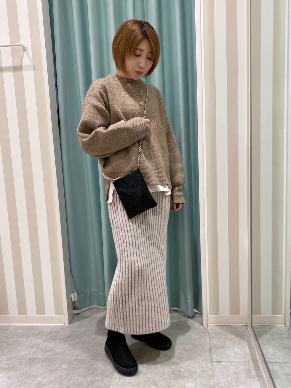 イエロー系のニット/セーター、ホワイト系のTシャツ/カットソー、ベージュ系のスカートを着用したレディースの冬コーディネートの1枚目の写真