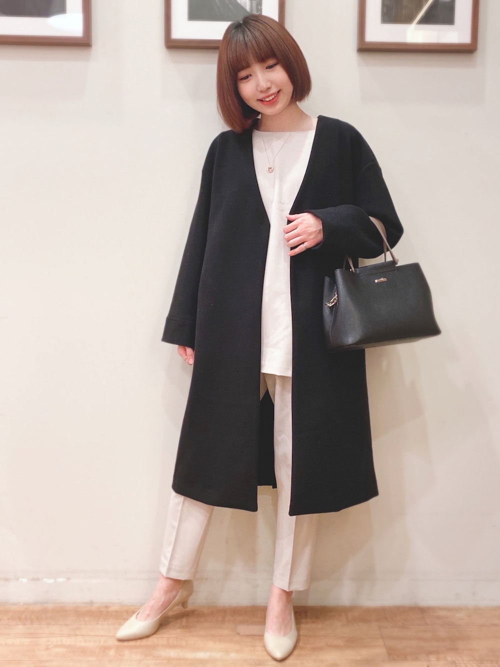 ブラック系のトートバッグ、ブラック系のノーカラーコート、ベージュ系のチュニックを着用したレディースの秋コーディネートの1枚目の写真