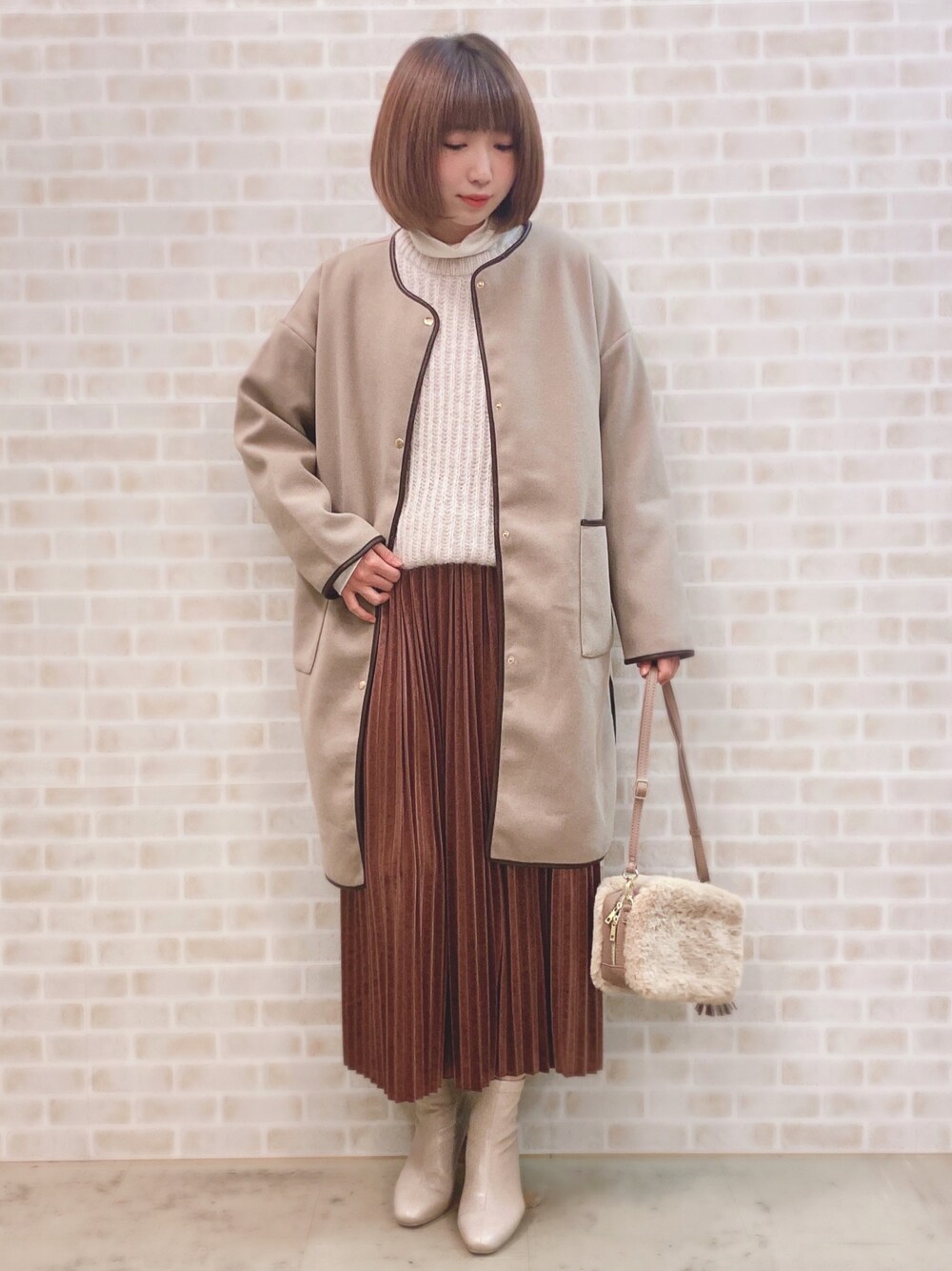 ベージュ系のノーカラーコート、ベージュ系のニット/セーター、ホワイト系のTシャツ/カットソーを着用したレディースの冬コーディネートの1枚目の写真