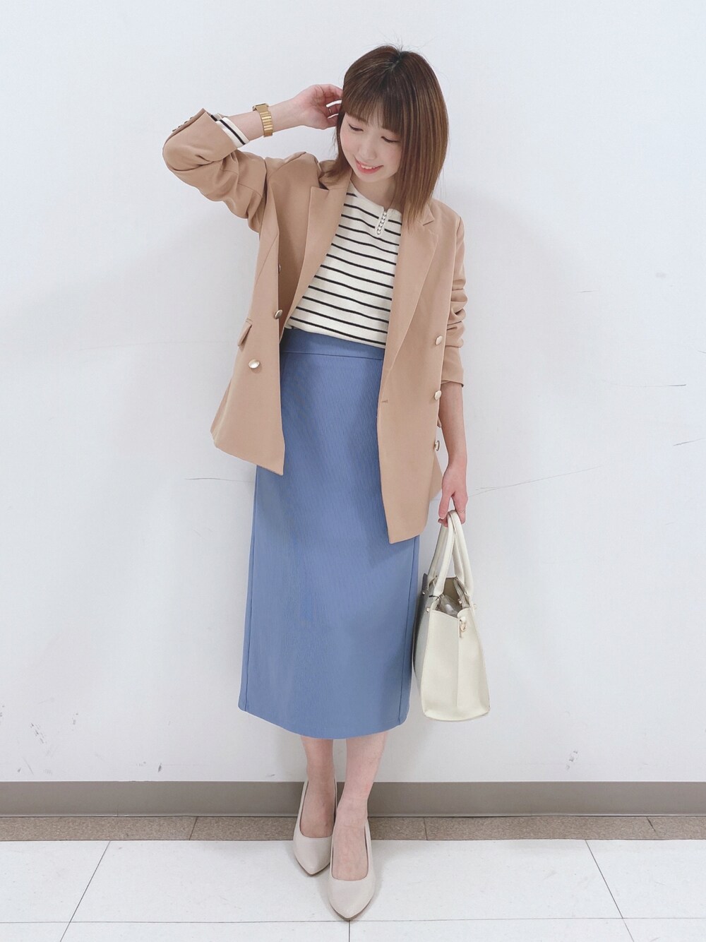 ベージュ系のテーラードジャケット、ホワイト系のニット/セーター、ブルー系のスカートを着用したレディースの冬コーディネートの1枚目の写真