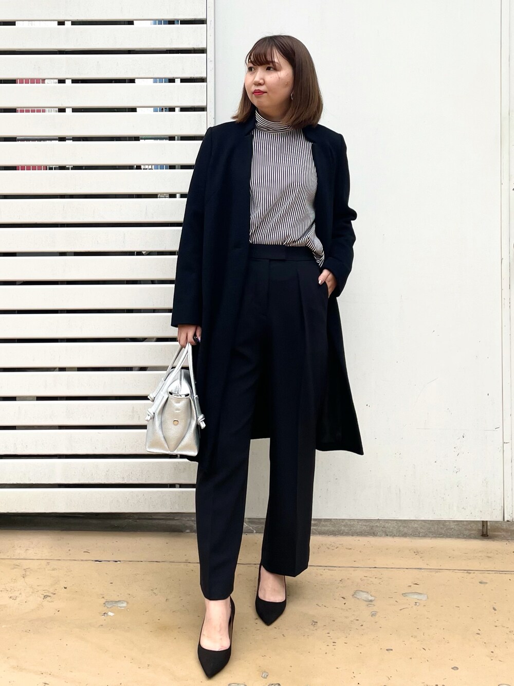シルバー系のハンドバッグ、ブラック系のパンプス、ブラック系のパンツを着用したレディースの秋コーディネートの1枚目の写真