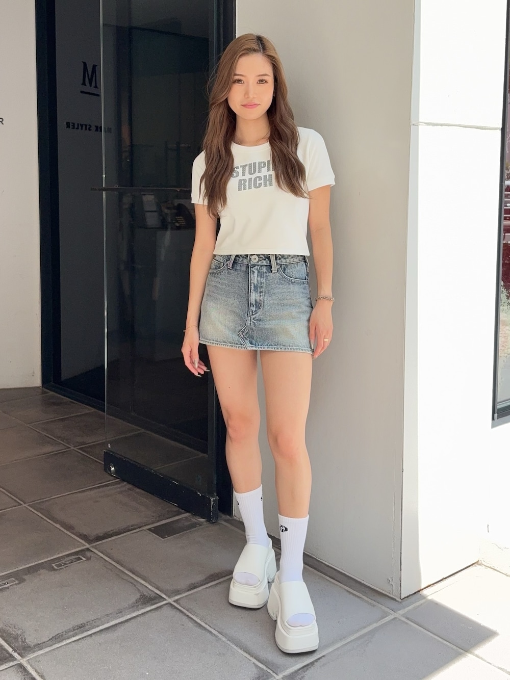 ホワイト系のTシャツ/カットソー、ブルー系のデニムスカート、ホワイト系のサンダルを着用したレディースの夏コーディネートの1枚目の写真