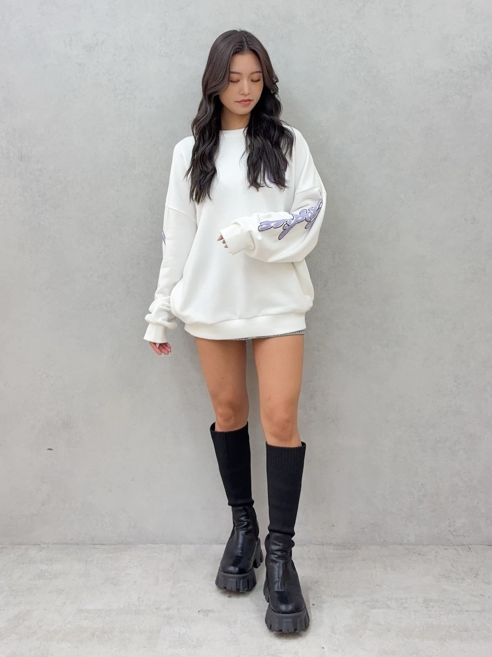 ホワイト系のスウェット、ブルー系のデニムスカート、ブラック系のブーツを着用したレディースの秋コーディネートの1枚目の写真