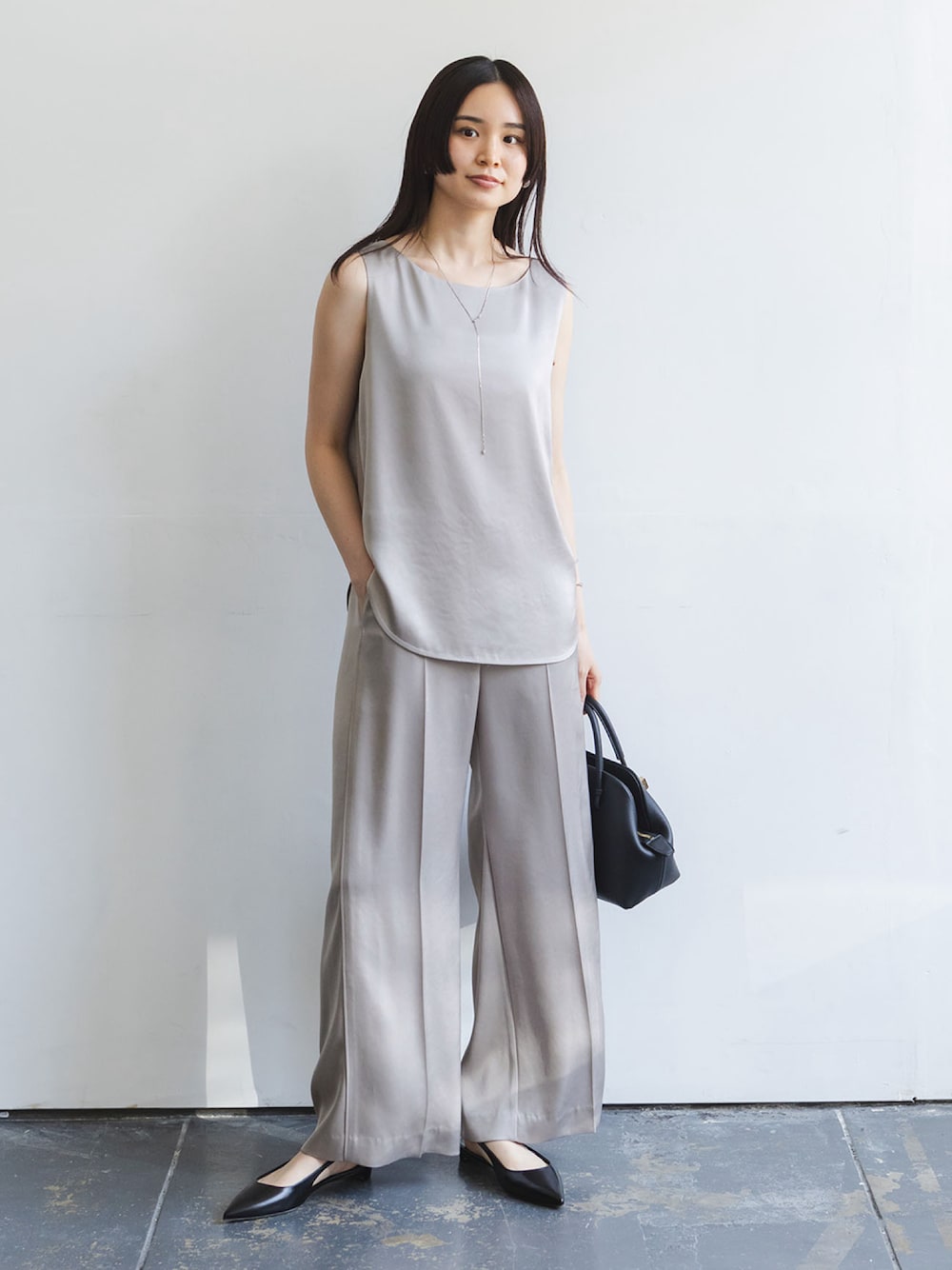 グレー系のタンクトップ、グレー系のスラックス、ブラック系のショルダーバッグを着用したレディースの秋コーディネートの1枚目の写真