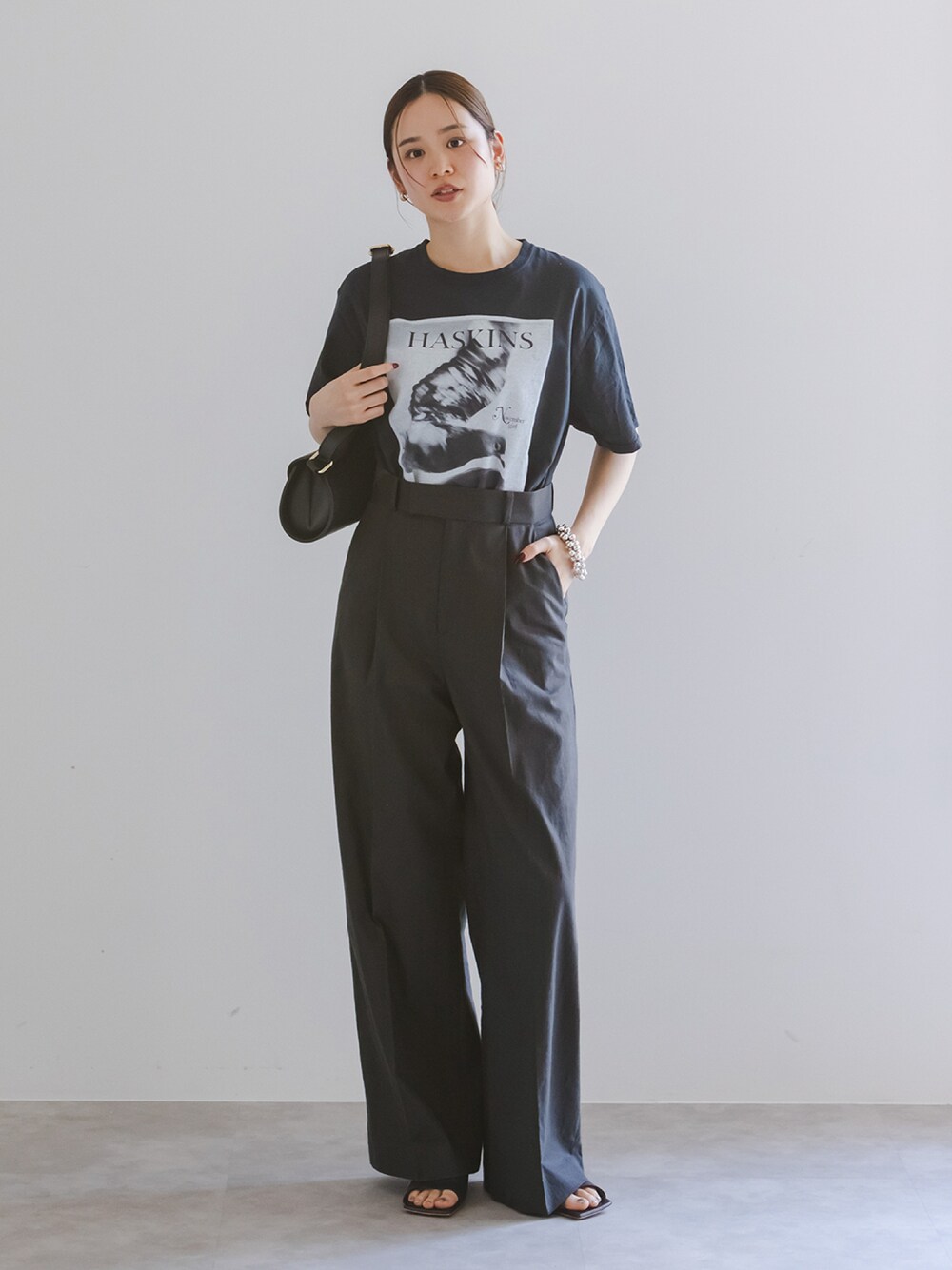 ブラック系のTシャツ/カットソー、グレー系のスラックス、ブラック系のショルダーバッグを着用したレディースの春コーディネートの1枚目の写真