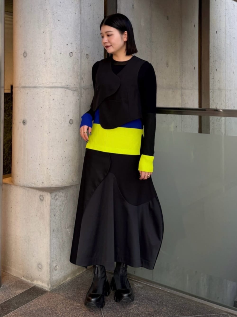 ブラック系のベスト、グリーン系のニット/セーター、ブラック系のスカートを着用したレディースの秋コーディネートの1枚目の写真