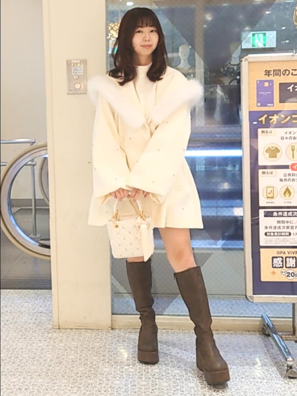 ホワイト系のノーカラーコート、ホワイト系のニット/セーター、ホワイト系のショルダーバッグを着用したレディースの冬コーディネートの1枚目の写真