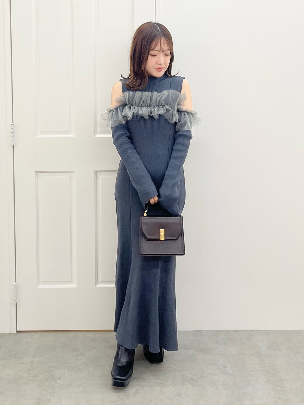グレー系のワンピース、ブラウン系のハンドバッグ、ブラック系のブーツを着用したレディースの秋コーディネートの1枚目の写真