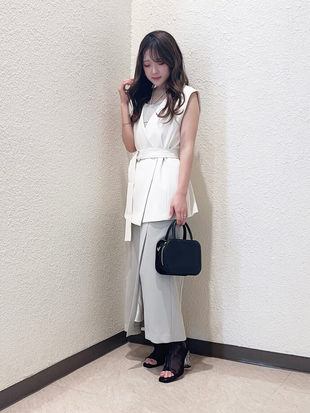 グリーン系のワンピース、ホワイト系のベスト、ブラック系のハンドバッグを着用したレディースの春コーディネートの1枚目の写真
