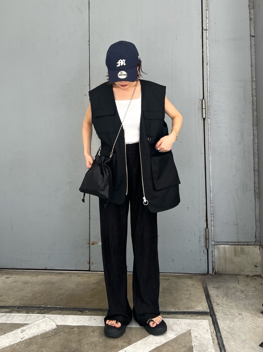 ブラック系のベスト、ホワイト系のニット/セーター、ブルー系のキャップを着用したレディースの夏コーディネートの1枚目の写真