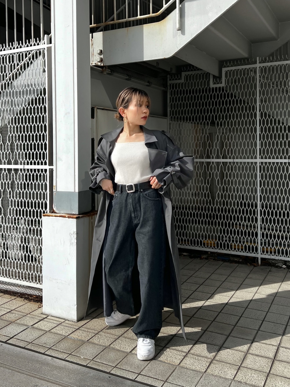 グレー系のトレンチコート、ブラック系のデニムパンツ、ブラック系のベルトを着用したレディースの冬コーディネートの1枚目の写真