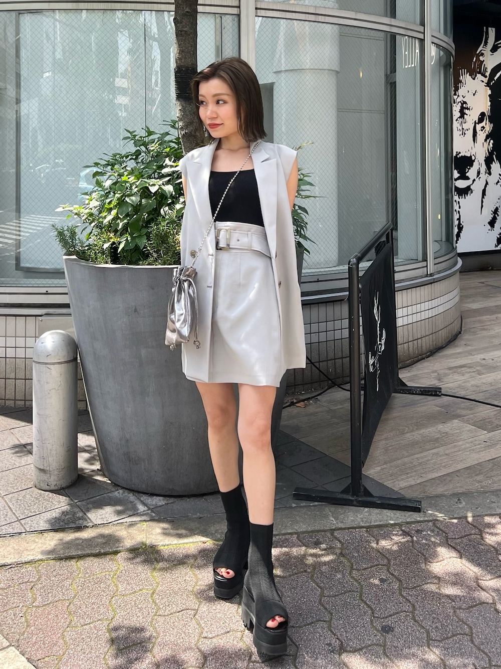 グレー系のベスト、ブラック系のブーツ、グレー系のスカートを着用したレディースの春コーディネートの1枚目の写真