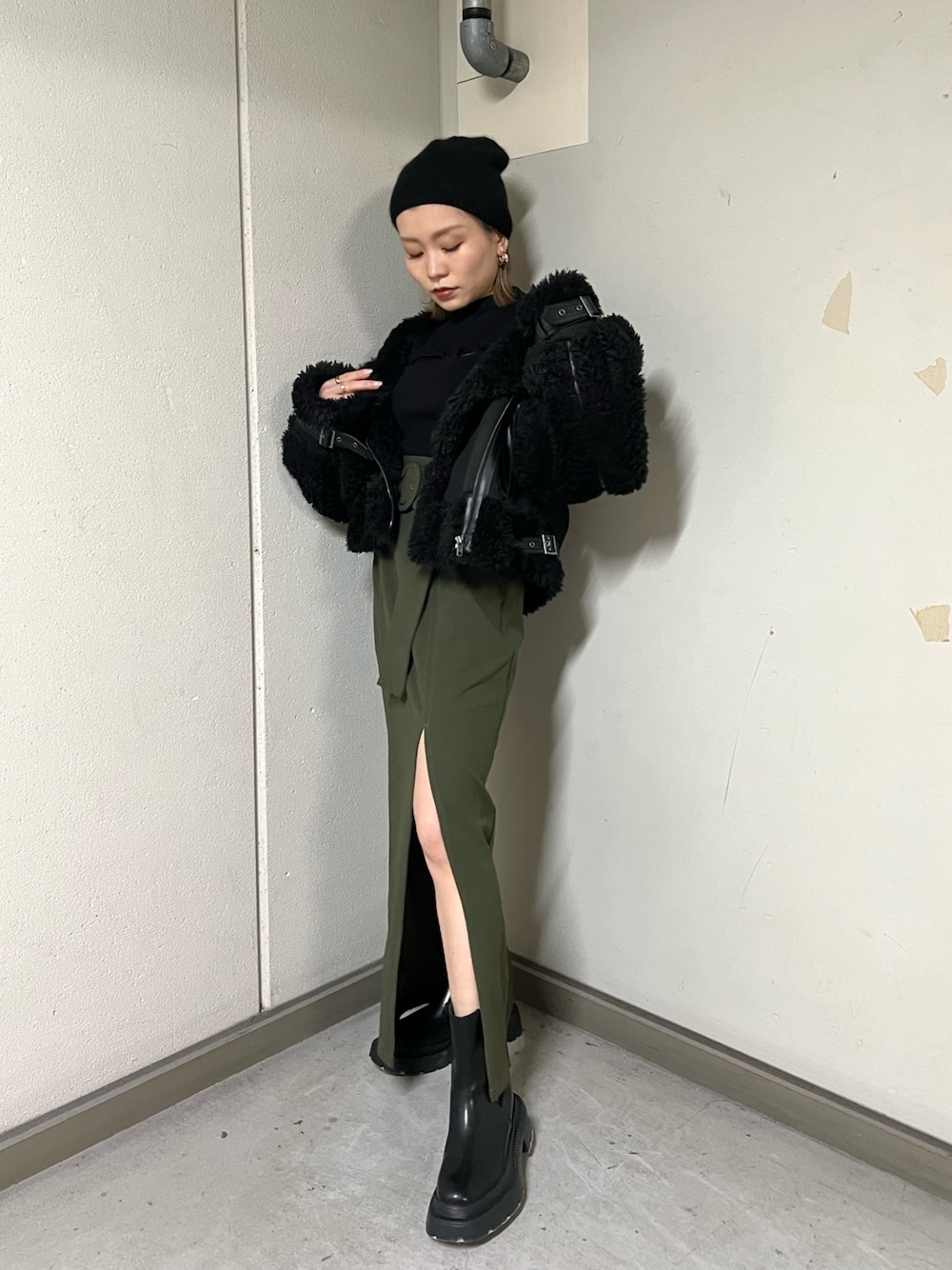 ブラック系のムートンコート、ブラック系のニット/セーター、グリーン系のスカートを着用したレディースの冬コーディネートの1枚目の写真