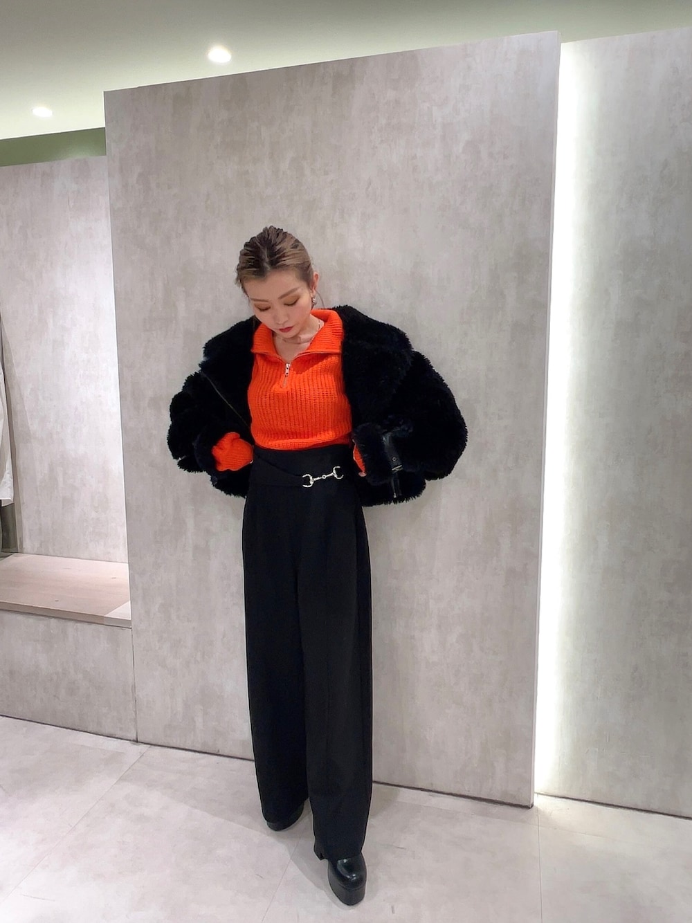 ブラック系のスラックス、オレンジ系のニット/セーター、ブラック系のムートンコートを着用したレディースの冬コーディネートの1枚目の写真