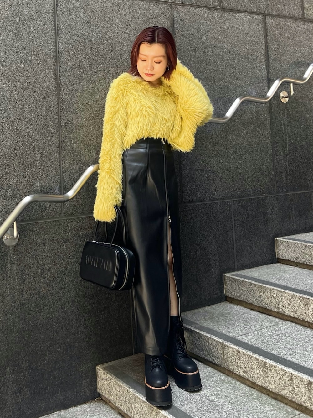 イエロー系のニット/セーター、ブラック系のスカート、ブラック系のブーツを着用したレディースの秋コーディネートの1枚目の写真