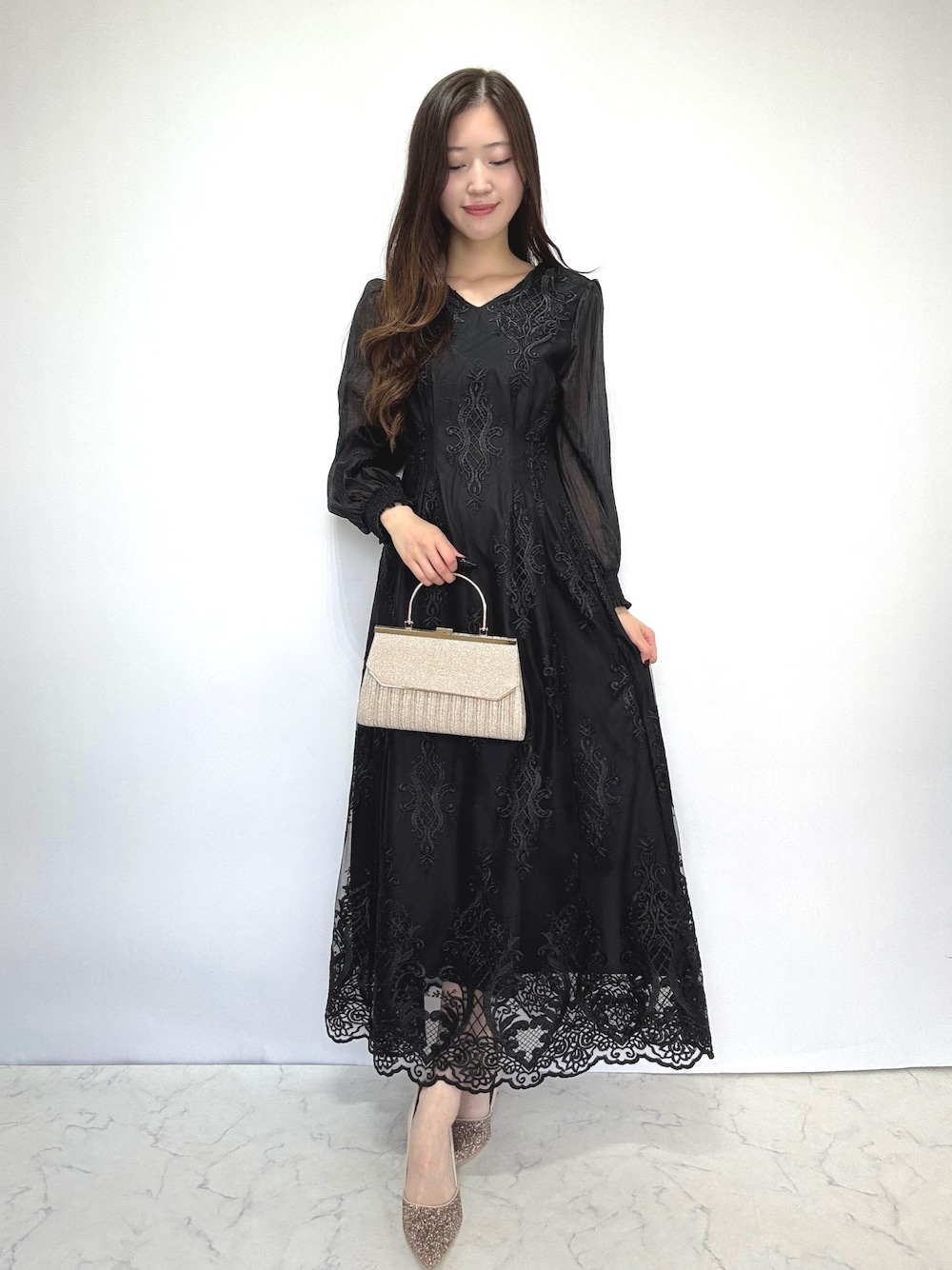 ベージュ系のクラッチバッグ、ベージュ系のパンプス、ブラック系のドレスを着用したレディースの秋コーディネートの1枚目の写真